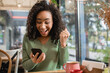 © LIGHTFIELD STUDIOS - excited african american woman with clenched fist looking at smartphone in cafe