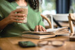 © LIGHTFIELD STUDIOS - cropped view of african american woman holding glass with latte while reading book in cafe