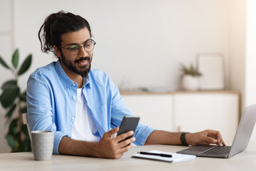Poster - Arab Freelancer Guy Using Smartphone While Working On Laptop In Home Office