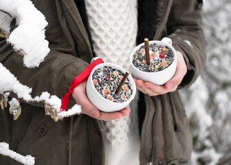 Young girl holding two homemade hanging teacups bird feeder in the winter garden. Help people to animals. Selective focus.