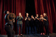 © standret - Standing against red curtains. Group of actors in dark colored clothes on rehearsal in the theater