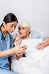 Sticker - excited senior woman showing idea gesture while using digital tablet together with astonished asian nurse