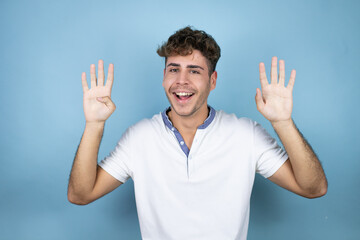 Young handsome man wearing a white t-shirt over blue background showing and pointing up with fingers number nine while smiling confident and happy