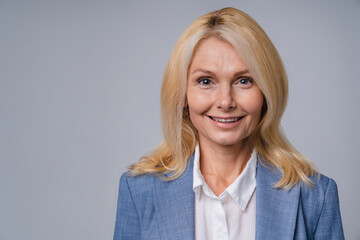 Blonde charming senior business woman in formal attire smiling and looks confident isolated over grey background