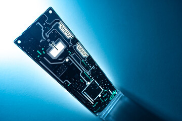 Poster - The PC Board is illuminated from the back. Computer components. The printed circuit Board stands vertically on the table. The electronic background.