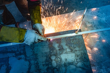 Wall Mural - Worker cuts metal. Metalworking concept. Laser cutting of metal. A man in a protective suit cuts a piece from a sheet of metal. Hands of a worker, a cutter, a sheet of steel and sparks.