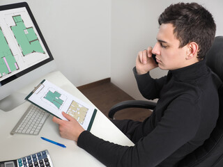 Poster - Construction engineer with a smartphone. Architect sits at his desk and communicates on his mobile phone. Man works with floor plans. Coordination of alterations in buildings. Civil engineer at work.