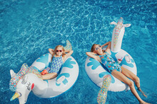 Cute Adorable Girls Sisters Friends With Drinks Lying On Inflatable Rings Unicorns. Kids Children Siblings In Sunglasses Having Fun In Swimming Pool. Summer Outdoors Water Activity For Kids.