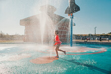 Cute Adorable Caucasian Funny Girl Playing On Splash Pad Playground On Summer Day. Happy Child Having Fun In Water. Seasonal Water Sport Recreational Activity For Kids Outdoors.
