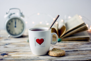 Canvas Print - Valentine's day breakfast. White mug of tea with red heart, alarm clock, biscuit heart, garland book on a wooden table. Romantic love background.