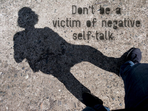 Wall Mural -  - Inspirational motivational quote  - Do not be a victim of negative self talk. On background of silhouette shadow of a person walking on the street.