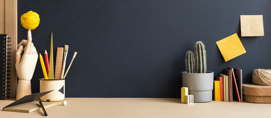 Creative desk with a blank picture frame or poster, desk objects, office supplies, books, cactus on a dark background. Banner.