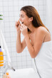 © LIGHTFIELD STUDIOS - young woman, wrapped in white towel, flossing teeth in bathroom, blurred foreground