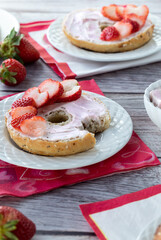 Bagel with a bite out covered in strawberry cream cheese and strawberry slices for Valentine's Day. 