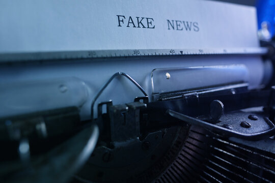 old typewriter on table, words fake news are printed on paper in large size, candle is burning, retro style, concept of information hoax in social media, misleading, exposing deception