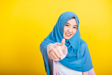 Wall Mural - Asian Muslim Arab, Portrait of happy beautiful young woman Islam religious wear veil hijab funny smile she made finger thumbs up, Ok sign to agree, studio shot isolated on yellow background