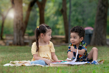 Boy and girl playing on lawn, cute little children sitting draw together in nature outdoor at park