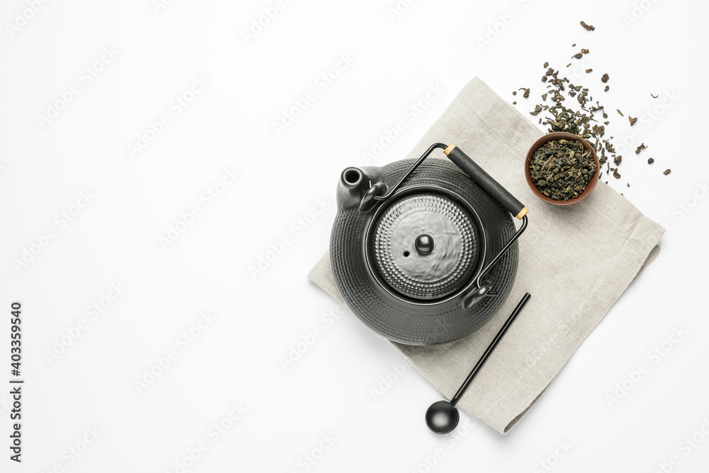 Composition with teapot, spoon and dry tea leaves on white background