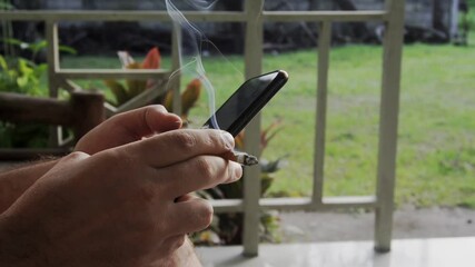 Close-up of a man typing a text message on a smartphone with a cigarette in his hand. Slow motion FullHD footage