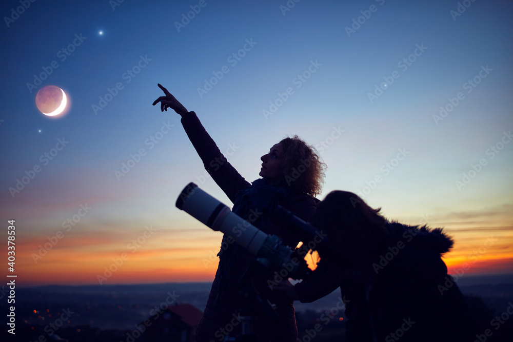 Mother and daughter observing stars, planets, Moon and night sky with astronomical telescope. - obrazy, fototapety, plakaty 