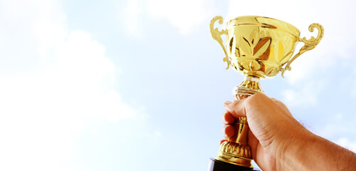 Wall Mural - man holding up a trophy cup as a winner against the blue sky. award and victory concept