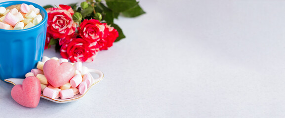 a pair of red heart candies next to a bouquet of roses and cup of coffee with marshmallows; gift of berry sweets or cakes for valentine's day, wedding or anniversary; romantic banner with copy space