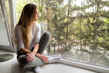 Frustrated sad girl sitting in front of window at home