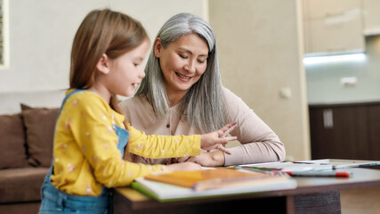 Grandmother staying at home with little granddaughter while drawing