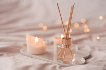 home aroma fragrance diffuser with burning candles on white tray in bed over glowing lights close up