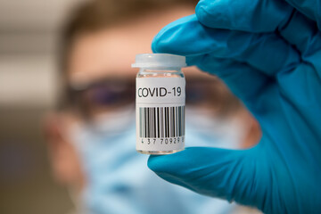 Coronavirus vaccination dose ready for immunisation. Doctor with gloved hands holding a glass vial of covid-19 vaccine