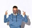 © FAB.1 - Headshot of serious mature grey-haired man in trendy sunglasses and casual sweatshirt aiming finger like gun pistol up. Studio portrait isolated on white background with copy space
