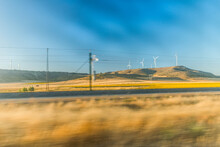 Speeding Across Train Tracks Looking Out Over Sunny Fields. Wind Farms In The Distance..