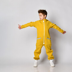 Studio portrait shot of little boy in yellow fleece sportswear showing thumbs-up and looking aside standing with arms and legs wide isolated on white background copy space