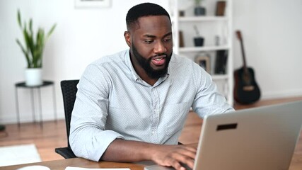 Involved African American typing on laptop, looks through working papers and taking notes. An intelligent multiracial man using computer for remote work indoor