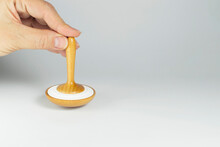 A Female Hand Holds A Wooden Whirligig Or Spinning Top Vertically On A Gray Background. Toy For Children. Close-up. Copy Space For Text.