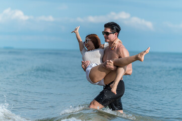 young man holding girlfriend and wading in ocean at the beach - sweet and funny lover couple