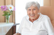 Smiling senior woman with an osteoporosis stoop in a comfy chair in her room at a retirement home.