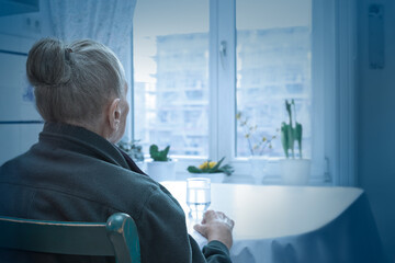 Loneliness concept, old-age depression: lonely old woman looking out of the window, blue filter effect.