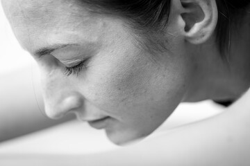 Close-up side view of a meditative young woman on a seated / forward bend or Sleeping Swan asana or yoga pose. Black and white horizontal view.