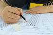 © Achira22 - Woman students hand holding pencil writing selected choice on answer sheets and Mathematics question sheets. students testing doing examination. school exam