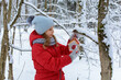 Girl hangs bird feeder on tree branch in winter snowy forest
