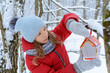 Girl hangs bird feeder on tree branch in winter snowy forest