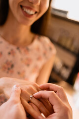 Wall Mural - Woman smiling, happy while her man Putting On Engagement Ring To Her Finger On A Romantic Date at home