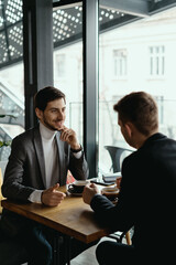 Two businessmen talking about new opportunities sitting with laptop at desk, planning project, considering business offer, sharing ideas