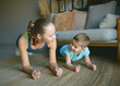 © MIKHAIL - mom and son play sports at home. they perform the plank exercise. a smile on their faces.