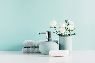 Soft light bathroom decor in mint color, towel, soap dispenser, white roses flowers, accessories on pastel mint background. Elegant decor bathroom interior