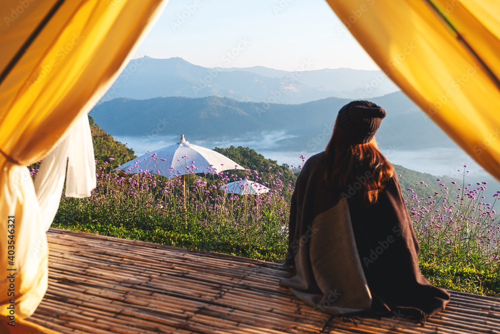 Rear view image of a woman sitting on wooden balcony while watching a beautiful mountains and nature view outside the tent - obrazy, fototapety, plakaty 
