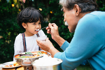 Grandfather feeding food to son in dinning party outdoor.