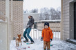 © Елена Григорович - Snow battle. Dad, son and their domestic dog playing snowballs during the snowfall in gray day. Outdoor winter family activity