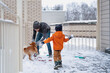 © Елена Григорович - Snow battle. Dad, son and their domestic dog playing snowballs during the snowfall in gray day. Outdoor winter family activity